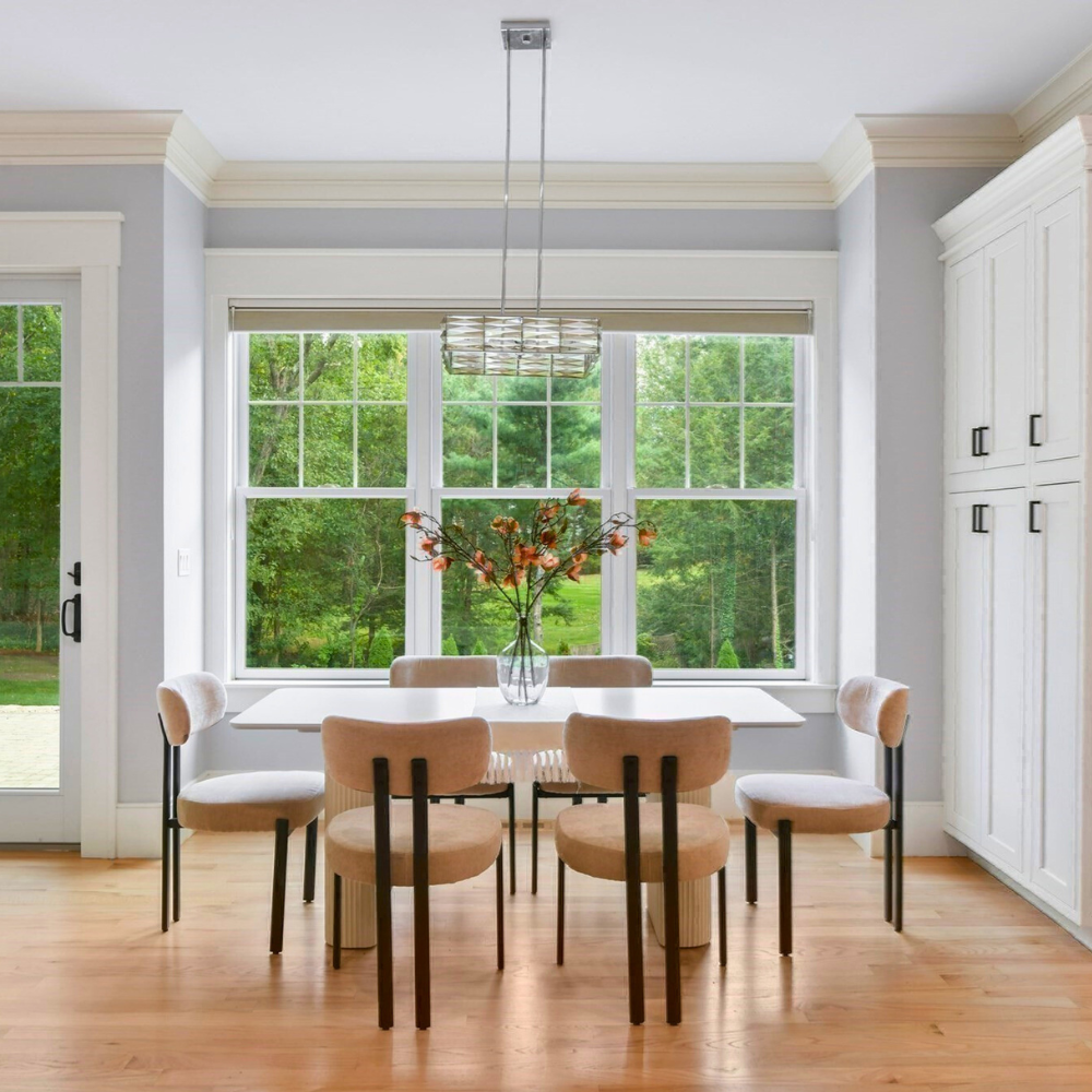 Dining room with a table and chairs near a large window with a view of greenery. Luxury staging in Wellesley, MA.