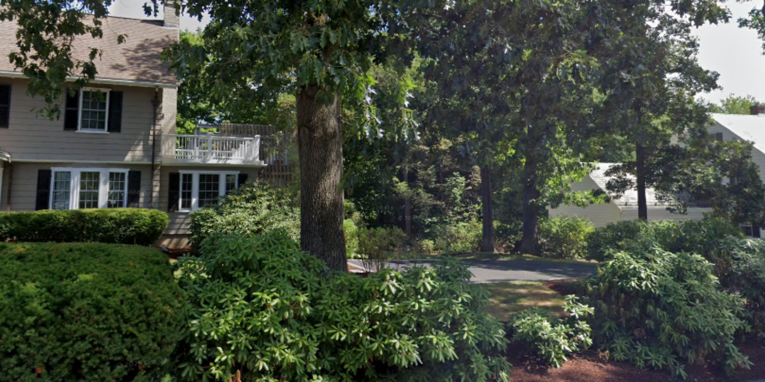 Lush green garden with trees and a house in the background. Offering luxury staging services in Wellesley, MA.