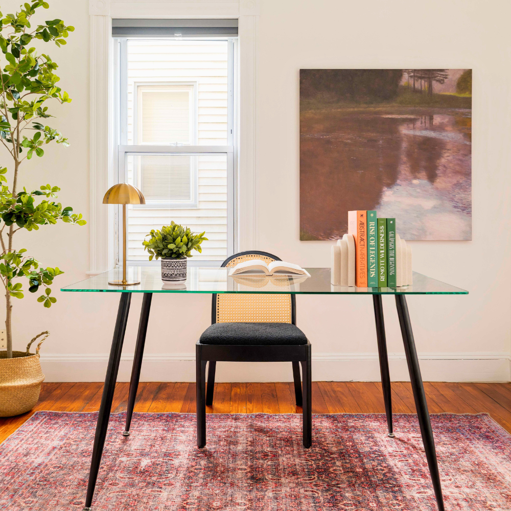 Glass dining table with black legs and a chair in a room with a painting on the wall. Luxury staging in Somerville, MA.